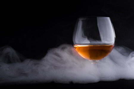Photo of cognac glass in a smoke against black backgroundの写真素材