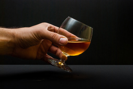 cognac glass in human hand against black backgroundの写真素材