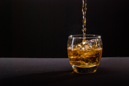whiskey pouring into glass against black backgroundの写真素材