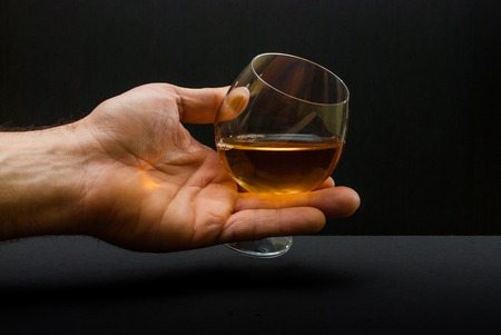 cognac glass in human hand against black backgroundの写真素材