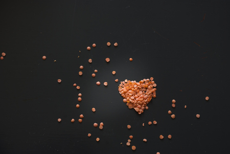 photo of red lentil heart on dark wooden tableの写真素材