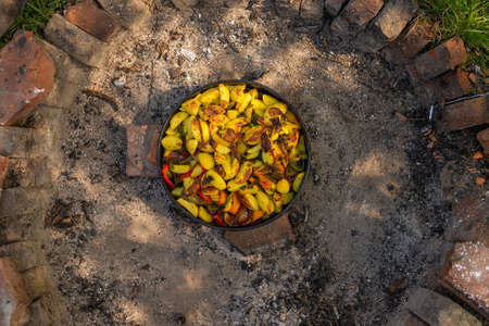 Photo of Cooking traditional dalmatian, croatian, bosnian dish called peka. Meat, potatoes and vegetables in pot and covered with hot charcoal and ash. Balkan food.の写真素材