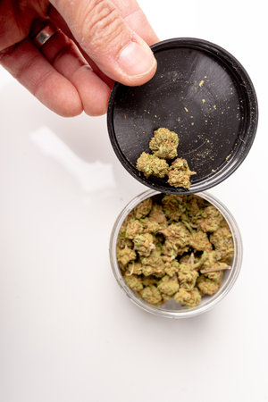 Photo of Jar cup with medical marijuana in the human hand. Marijuana buds, cannabis dried flowers. White table as background.の写真素材