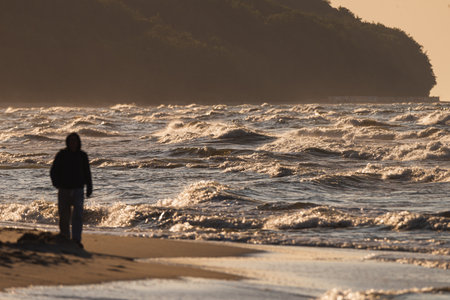 Photo of Unrecognized human watching stormy waves on Baltic Sea. golden hour.