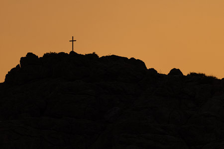 Photo of Catholic Cross on top of the rocky mountain at sunset.の写真素材