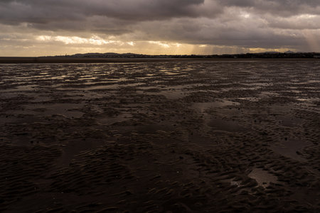 Dramatic, moody atmosphere over Sandymount Beach, Dublin, Ireland. Vast foreground of wet tidal flats reflects the dark, stormy clouds. Light breaks through on the distant horizon.の写真素材