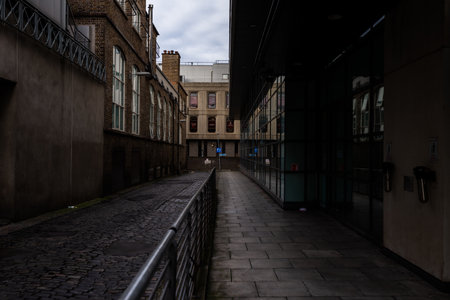 Atmospheric, moody alleyway in Dublin, Ireland. Strong contrast between an old, dark brick wall and a sleek, modern glass office building. Cobblestone street and dramatic light.の写真素材