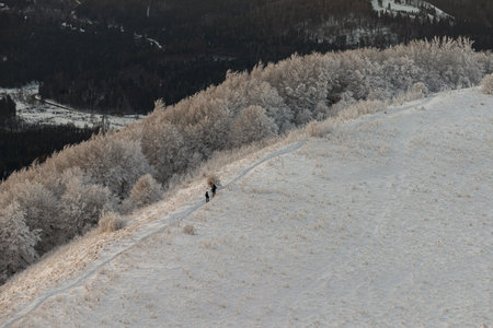 Two hikers walking along a snowy mountain ridge path surrounded by frosted trees in Bieszczady...