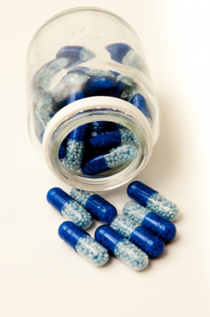 Blue pills spill out of a white containerの写真素材