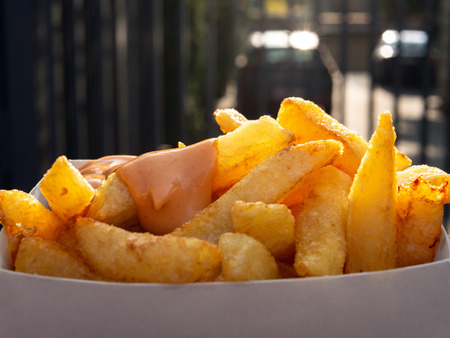 Box of french fries with sauce. Close-up on a box of french fries with sauce. Day light, blurry background behind. Concept of fast and unhealthy food.の写真素材