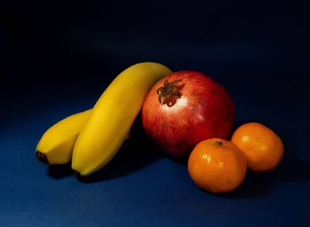 Pomegranate, bananas and mandarins. Still life on a dark background. Studio shot.