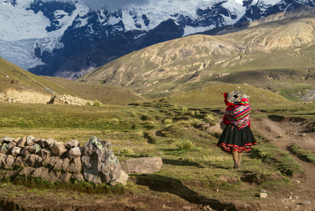A Peruvian woman walking with a child on her back in South American Andes
