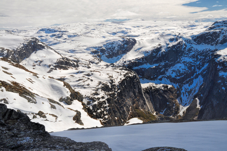 View from the top of mountain into a gorge in Norwegian mountains covered in moss and snow, near Trolltungaの写真素材