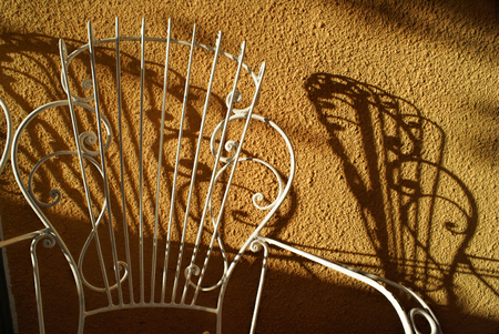 Picturesque view of a white garden chair casting a shadow on terracotta wallの写真素材