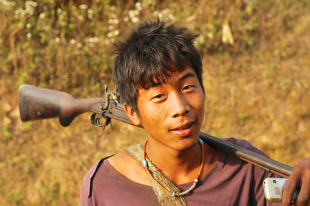 Nagaland, India - March 2012: Young man with rifle and mobile phone in Nagaland, remote region of India. Documentary editorial.のeditorial素材