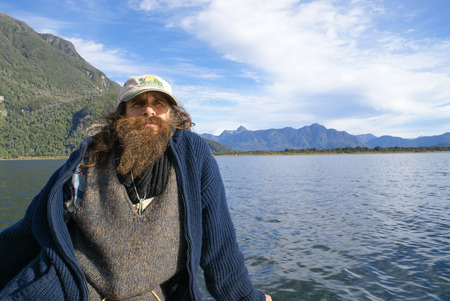Cagalandia, Chile - October 2008: Old man sits on sailing boat and focuses his eyes on horizon of beautiful countryside in Cagalandia, Chile. Documentary editorial.のeditorial素材