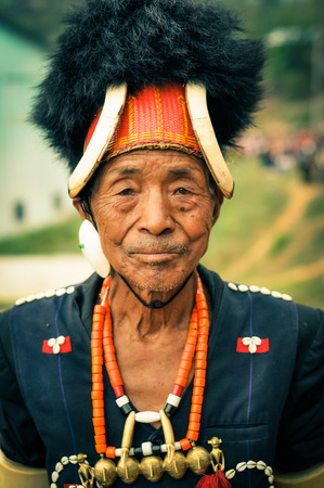 Mon, Nagaland - April 2012: Old native man with traditional large hat with fur and bones wears necklace made of beads and looks to photocamera at Aoleang festival in Mon, Nagaland. Documentary editorial.のeditorial素材
