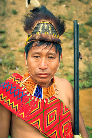 Mon, Nagaland - April 2012: Native man in costume with large hat made of fur holds his rifle and looks to photocamera at Aoleang festival in Mon, Nagaland. Aoleang is main festival of Konyaks from northern Nagaland. Documentary editorial.のeditorial素材