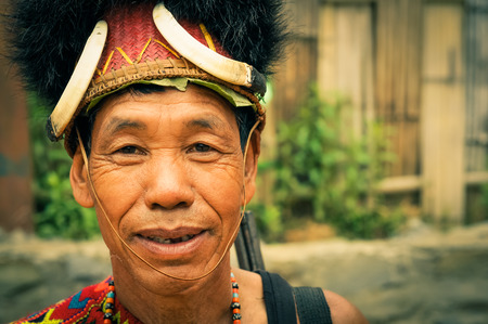Mon, Nagaland - April 2012: Man with wrinkles around his eyes wears traditional hat made of fur and looks nicely to photocamera at Aoleang festival in Mon, Nagaland. This festival showcases rich cultural heritage of this country. Documentary editorial.のeditorial素材