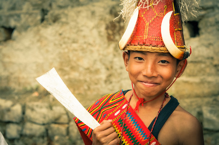 Mon, Nagaland - April 2012: Photo of smiling young boy with typical large hat with bones in traditional costume at Aoleang festival in Mon, Nagaland. Documentary editorial.のeditorial素材