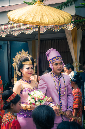 Makale, Indonesia - May 2015: Photo of beautiful bride and groom dressed in costumes of violet colour with golden jewellery during their wedding in Makale, capital city of Tana Toraja Regency, South Sulawesi, Indonesia. Bride holds bouquet of flowers and のeditorial素材