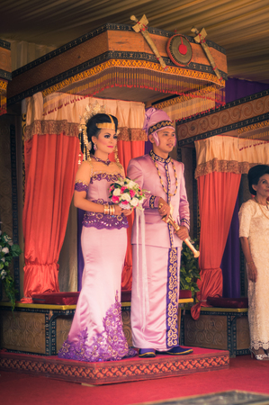 Makale, Indonesia - May 2015: Wedding couple, bride and groom, dressed in costumes of violet colour with golden jewellery pose during their wedding in Makale, capital city of Tana Toraja Regency, South Sulawesi, Indonesia. Bride holds bouquet of flowers aのeditorial素材