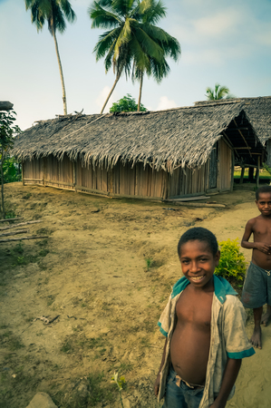 Will-will, Papua New Guinea - July 2015: Young boys smile and pose to photocamera near simple house made of wood in Will-will, Nuku, Papua New Guinea. Documentary editorial.のeditorial素材