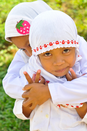 Katupat, Indonesia - June 2015: Two small children in white clothes hug and look to photocamera in Katupat, Sulawesi, Indonesia. Documentary editorial.のeditorial素材