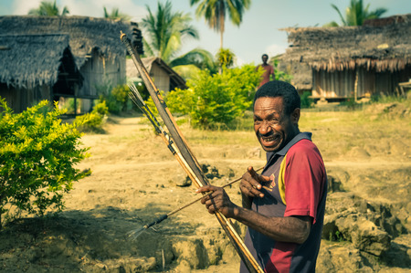 Will-will, Papua New Guinea - July 2015: Native man holds wooden bow and arrow and smiles with his finger aiming to photocamera in Will-will, Nuku, Papua New Guinea. Documentary editorial.のeditorial素材