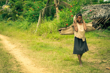 Will-will, Papua New Guinea - July 2015: Native woman in brown skirt carries load on her back with help of her head and smiles to photocamera in beautiful greenery in Will-will, Nuku, Papua New Guinea. Documentary editorial.のeditorial素材