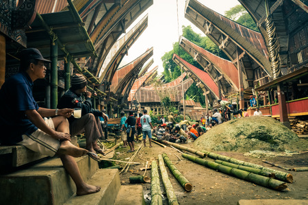 Toraja, Indonesia - June 2015: People sit in front of their houses and work with trunks of bamboo tree in Toraja, Sulawesi region, Indonesia. In centre with big stone. Documentary editorial.のeditorial素材