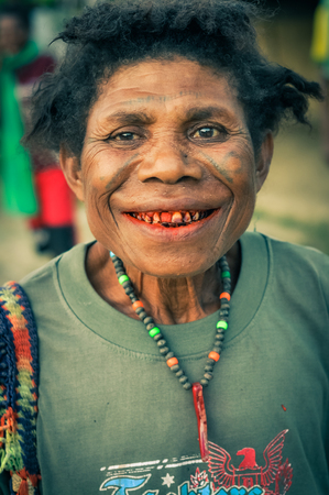 Will-will, Papua New Guinea - July 2015: Native woman with brown eyes and tattoos on her face wears necklace made of beads and smiles to photocamera in Will-will, Nuku, Papua New Guinea. Documentary editorial.のeditorial素材