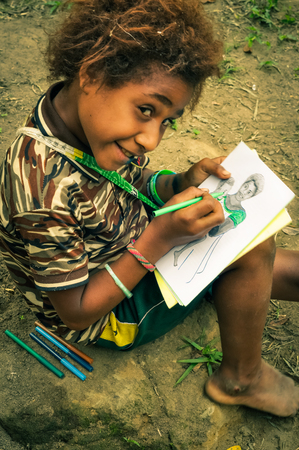 Will-will, Papua New Guinea - July 2015: Young sitting girl draws picture of mother with child and looks curiously up to photocamera in Will-will, Nuku, Papua New Guinea. Documentary editorial.のeditorial素材