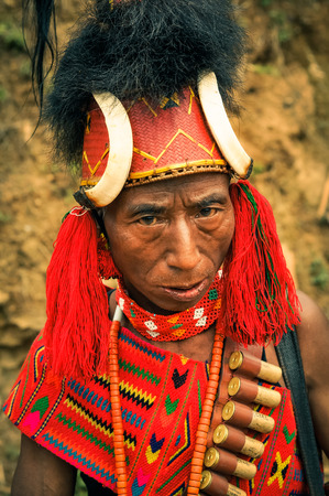 Mon, Nagaland - April 2012: Older native man with large hat with fur and bones dressed in colourful costume looks to photocamera at Aoleang festival in Mon, Nagaland. Documentary editorial.のeditorial素材