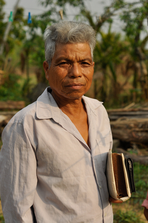 Cherapunjee, Meghalaya - March 2012: Old native man with grey hair dressed in white shirt holds book and looks to photocamera near Cherapunjee, Meghalaya. Documentary editorial.のeditorial素材