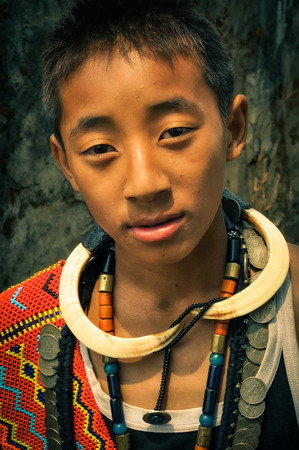 Wanching, Nagaland - April 2012: Young native boy wears traditional necklaces made of beads and other material and looks to photocamera during Aoleang festival in Wanching, Nagaland. Documentary editorial.のeditorial素材