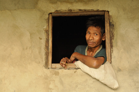 Cherapunjee, Meghalaya - March 2012: Native man with black hair smokes cigarette in window of his house and looks to photocamera near Cherapunjee, Meghalaya. Documentary editorial.のeditorial素材