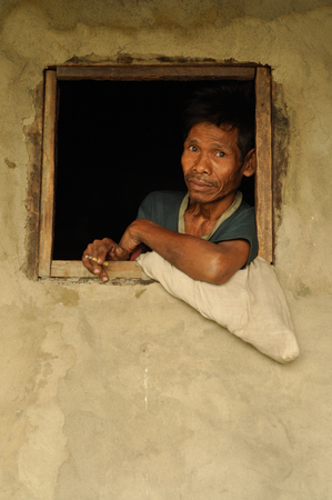 Cherapunjee, Meghalaya - March 2012: Photo of native man with black hair smoking cigarette in window of his house near Cherapunjee, Meghalaya. Documentary editorial.のeditorial素材