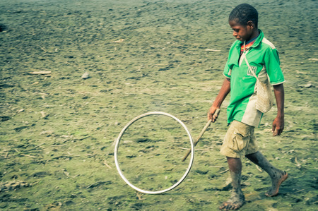 Palembe, Papua New Guinea - July 2015: Barefoot boy in green shirt plays with circle on field in Palembe, Sepik river, Papua New Guinea. Documentary editorial.のeditorial素材