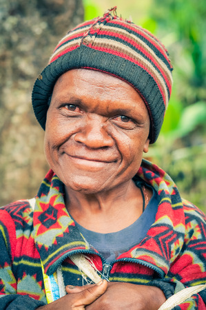 Kubor Range, Papua New Guinea - July 2015: Native woman with colourful cap and sweatshirt smiles nicely to photocamera in Kubor Range, Papua New Guinea. Documentary editorial.のeditorial素材