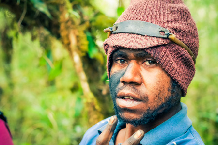 Sara village, Papua New Guinea - July 2015: Native boy with knitted cap and tattoo on his face looks to photocamera at Sara village in Papua New Guinea. Documentary editorial.のeditorial素材