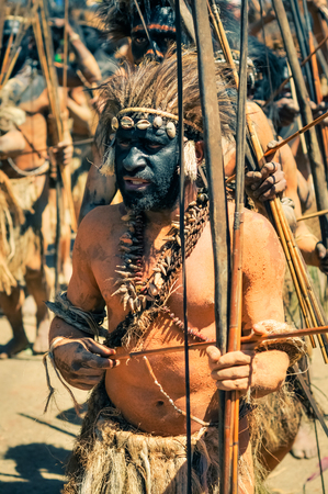 Wabag, Papua New Guinea - August 2015: Native half-naked man with black colour on face holds arrow and bow and wears headband with feathers during traditional Enga cultural show in Wabag, capital of Enga Province, Papua New Guinea. Documentary editorial.のeditorial素材