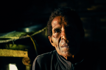 Kubor Range, Papua New Guinea - August 2015: Native man looks left in dark room in Kubor Range, Papua New Guinea. Documentary editorial.のeditorial素材