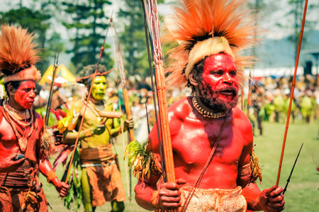 Hagen show, Papua New Guinea - circa August 2015: Native man with body covered in red colour wears cap made of fur and feathers and dances during Hagen show, Papua New Guinea. Documentary editorial.のeditorial素材