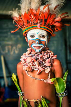 Hagen show, Papua New Guinea - circa August 2015: Young native boy with hat made of feathers smiles nicely during preparation for Hagen show, Papua New Guinea. Documentary editorial.のeditorial素材