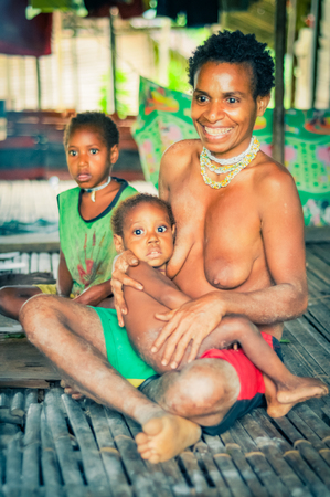 Dekai, Indonesia - September 2015: Naked native woman poses with her small childred and smiles joyfully looking ahead in Dekai, Papua, Indonesia. Documentary editorial.のeditorial素材
