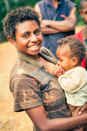 Kubor Range, Papua New Guinea - circa July 2015: Native woman in brown shirt breastfeeds her child in Kubor Range, Papua New Guinea. Documentary editorial.のeditorial素材