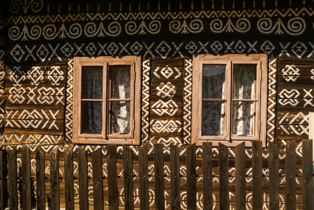 Old wooden house with two windows and many white ornaments painted on its wall in Cicmany, old village in Slovakia.の写真素材