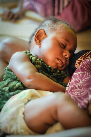 Palembe, Papua New Guinea - July 2015: Small sleeping child in arms of his mother in Palembe, Sepik river, Papua New Guinea. Documentary editorial.のeditorial素材