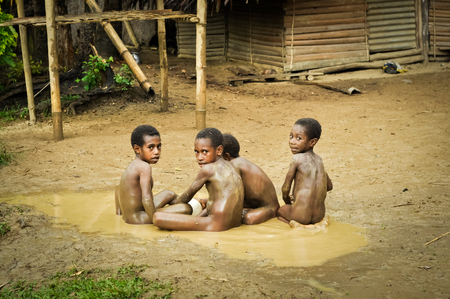 Will-will, Nuku, Papua New Guinea - July 2015: Small naked boys sit on ground and play in mud in Will-will in Nuku, Papua New Guinea. In this region, one can only meet people from isolated local tribes. Documentary editorial.のeditorial素材